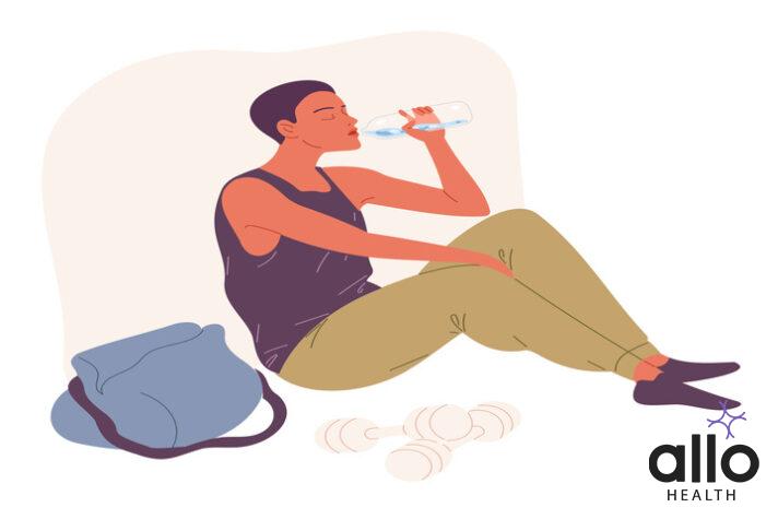 Young man sits on the floor and drinks water with dumbles in the front.