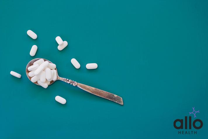 use of doxinate tablet in pregnancy in hindi. Overhead shot of a spoon full of white pills on a teal background.