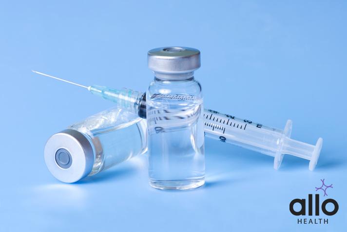 clindamycin injection uses in hindi. Syringe and vials of injectable medication on blue.